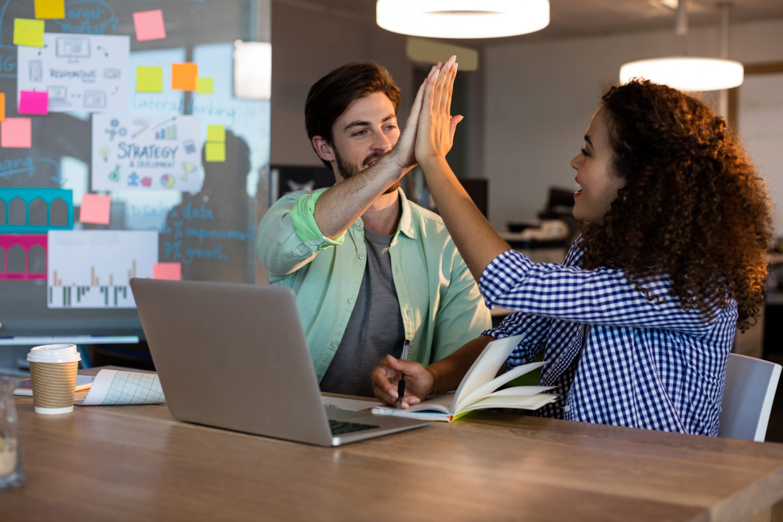 Creative business people giving high five to each other at desk in office
